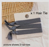 Three grey elastic hair ties, tied around a white presentation backing card, partially resting on a straw table mat and white table cloth
