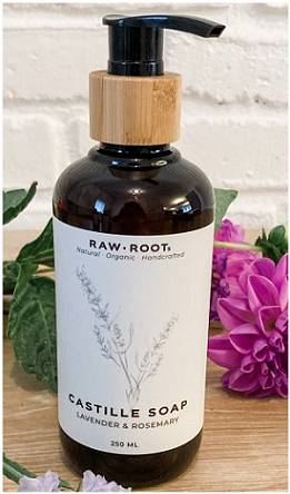 A 250 millilitre bottle of Lavender and Rosemary scented RAW ROOTS Natural Organic Castille Shampoo/Soap displayed on a wooden table top with flowers in front and behind