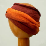 A Fair Trade Tie Dye Stretch Cotton Dreadlock Headwrap/Dreadwrap in Orange and Brown colours shown on wooden mannequin head