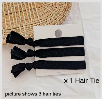 Three black elastic hair ties, tied around a white presentation backing card, partially resting on a straw table mat and white table cloth