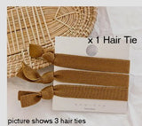 Three brown elastic hair ties, tied around a white presentation backing card, partially resting on a straw table mat and white table cloth