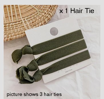 Three green elastic hair ties, tied around a white presentation backing card, partially resting on a straw table mat and white table cloth