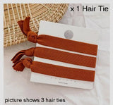 Three rust coloured elastic hair ties, tied around a white presentation backing card, partially resting on a straw table mat and white table cloth