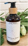 A 250 millilitre bottle of Sage and Lime scented RAW ROOTS Natural Organic Castille Shampoo/Soap displayed on a wooden table top with flowers in front and behind